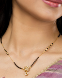 Close-up of a woman wearing a gold necklace with black beads.