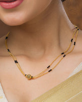 Close-up of a woman wearing a gold necklace with black beads.