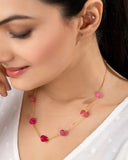 Woman wearing a gold necklace with pink gemstones on a neutral background