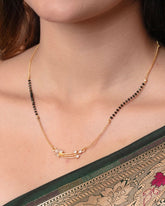 Necklace with black beads and gold chain worn by a person, with a patterned fabric background.