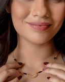 Woman wearing a gold necklace with black beads, close-up of her neck and hands.