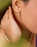 Close-up of a person wearing gold earrings with a blurred green background