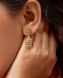 Close-up of a person wearing gold earrings with intricate designs.