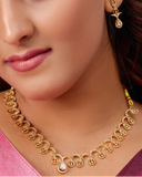 Woman wearing gold jewelry including a necklace and earrings against a dark background