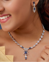 Woman wearing a necklace and earrings with a blue gemstone on a blurred background