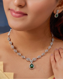 Woman wearing a silver necklace with a green gemstone and matching earrings.