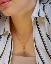 Close-up of a person wearing a gold necklace with a pineapple pendant, against a blurred background.
