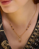 Gold necklace with a pendant on a person wearing a black and gold patterned top.