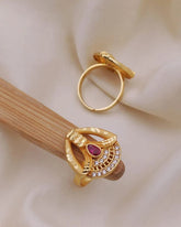 Gold ring with a red gemstone on a beige surface