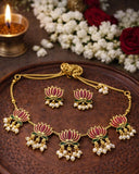 Gold jewelry set with pink floral design on a wooden surface with flowers and a candle.