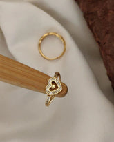 Gold ring with heart design on a wooden stand against a neutral background