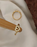 Gold ring with heart design on a wooden stand against a neutral background