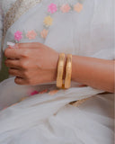 Gold bangles on a hand with a white saree with floral embroidery in the background