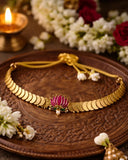 Gold necklace with a pink flower design on a wooden tray surrounded by flowers and a lit candle.