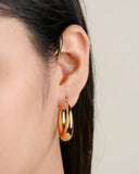Gold hoop earring worn by a person with dark hair on a neutral background