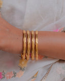 Gold bangles on a wrist with a floral dress in the background