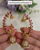 Gold peacock earrings with pink stones held by a hand against a light background.