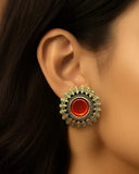 Close-up of a woman wearing a gold earring with a red gemstone against a neutral background