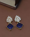 Pair of earrings with blue square stones and gold accents on a brown background