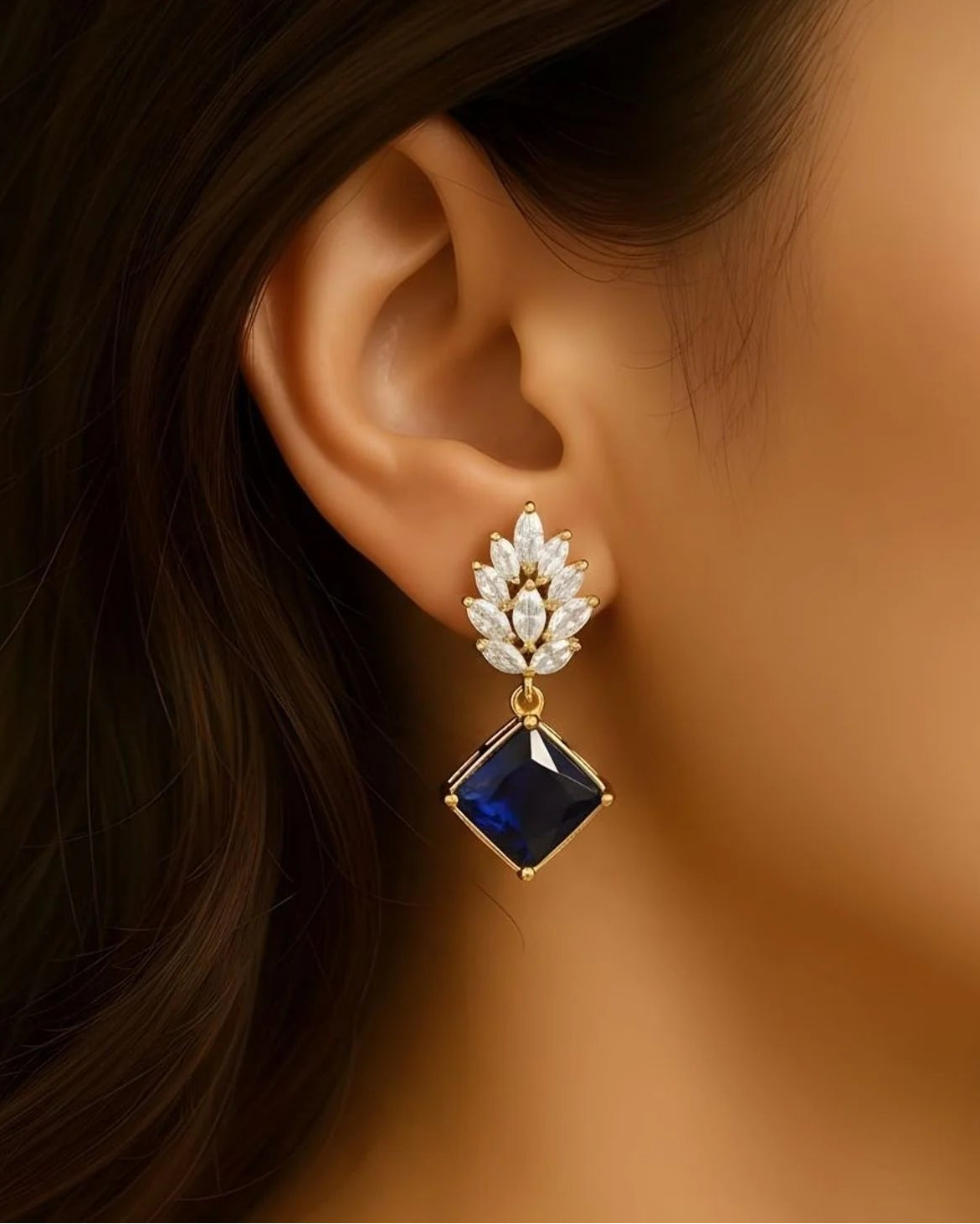 Close-up of an ear wearing a decorative earring with a blue gemstone and gold accents.