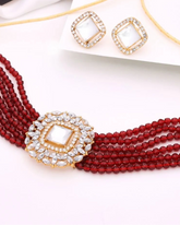 Jewelry set with red beaded necklace and gold earrings on a white fabric background