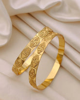 Two gold bangles with intricate patterns on a beige fabric background