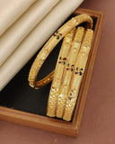 Three gold bangles with intricate designs on a reflective surface
