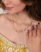 Woman wearing a gold necklace with a close-up of her hand and jewelry.