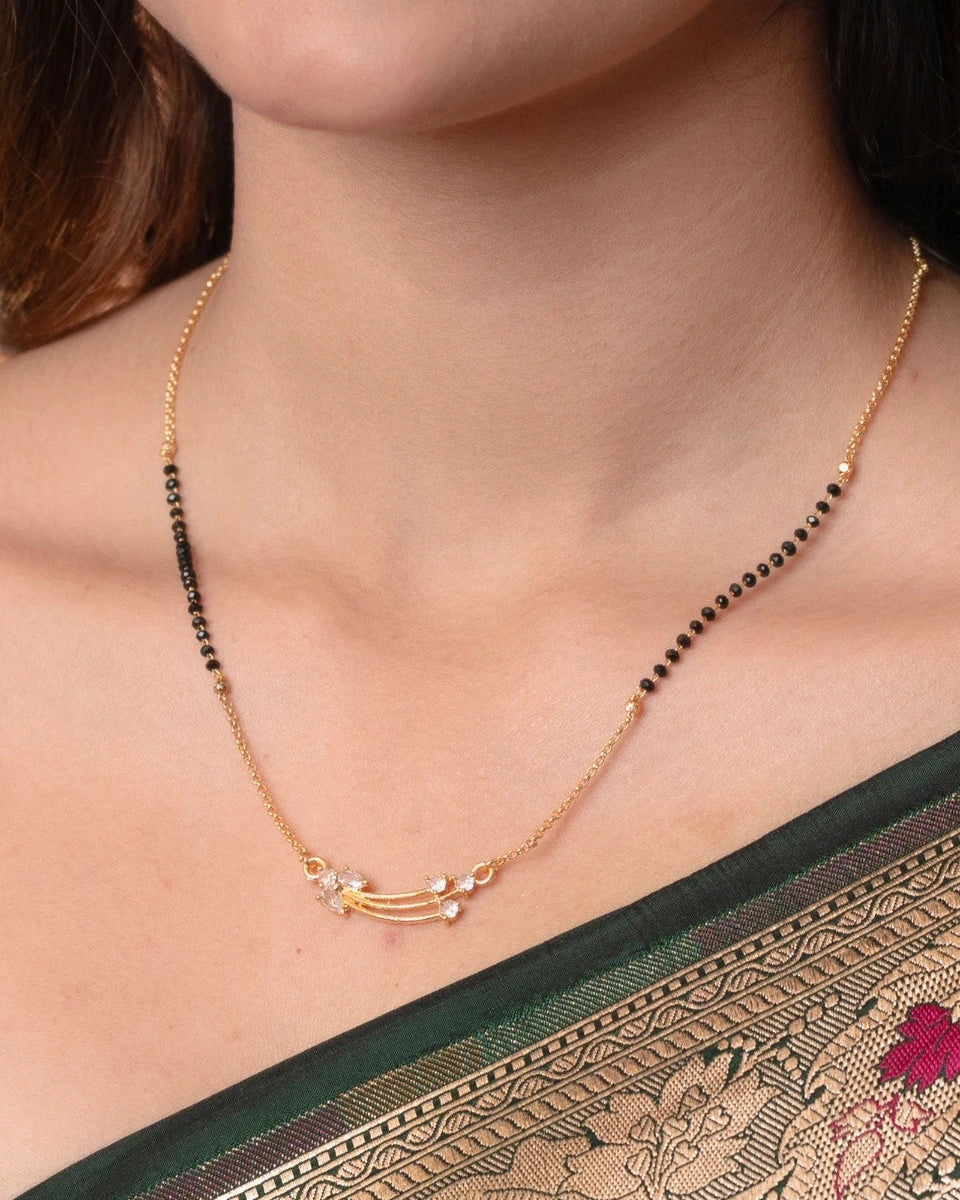 Necklace with black beads and gold chain worn by a person, with a patterned fabric background.