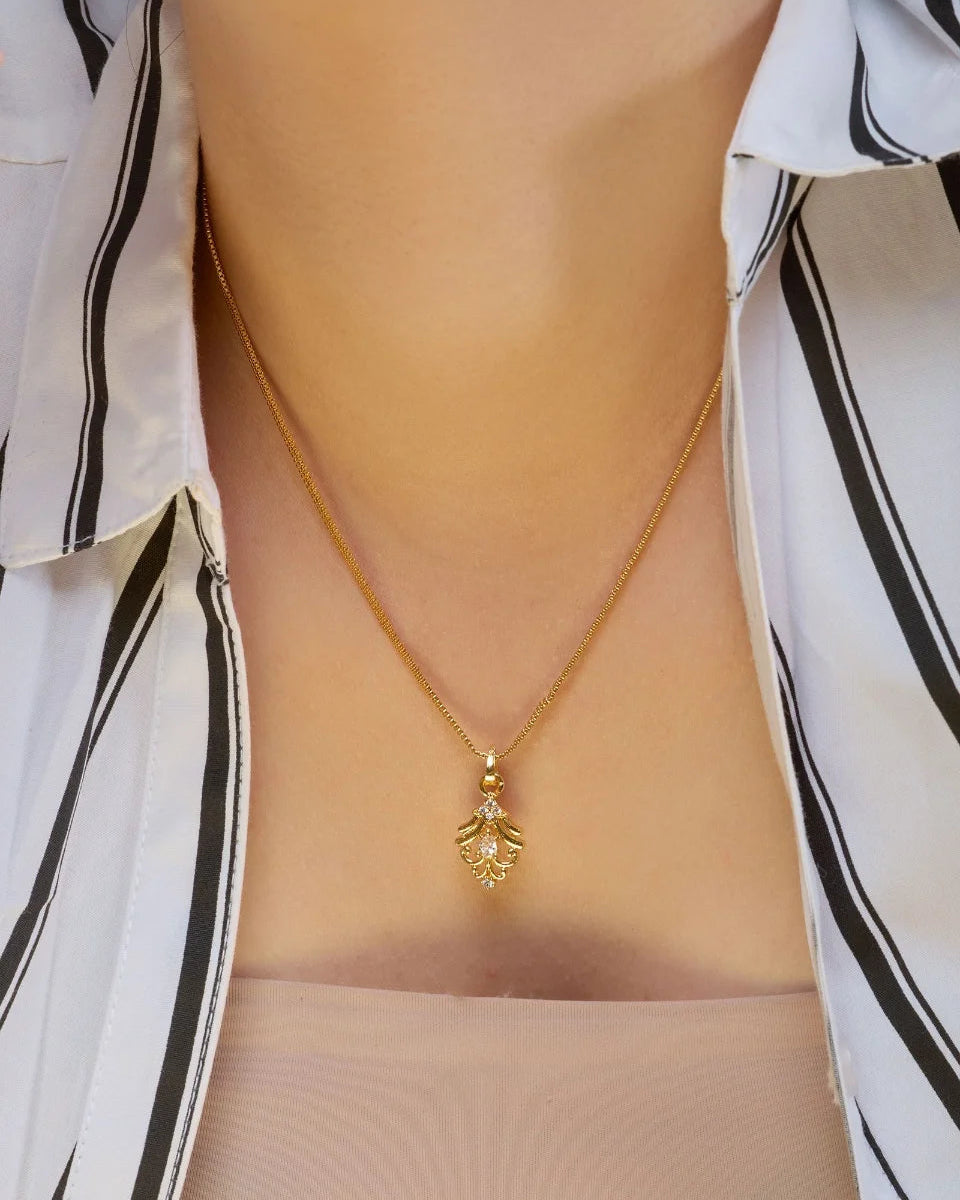 Gold necklace with a pendant worn by a person wearing a white shirt with black stripes.