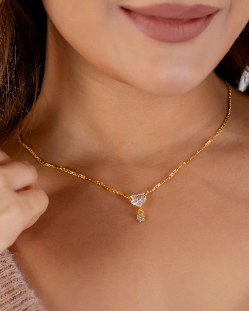 Close-up of a gold necklace with a heart-shaped pendant worn by a person.