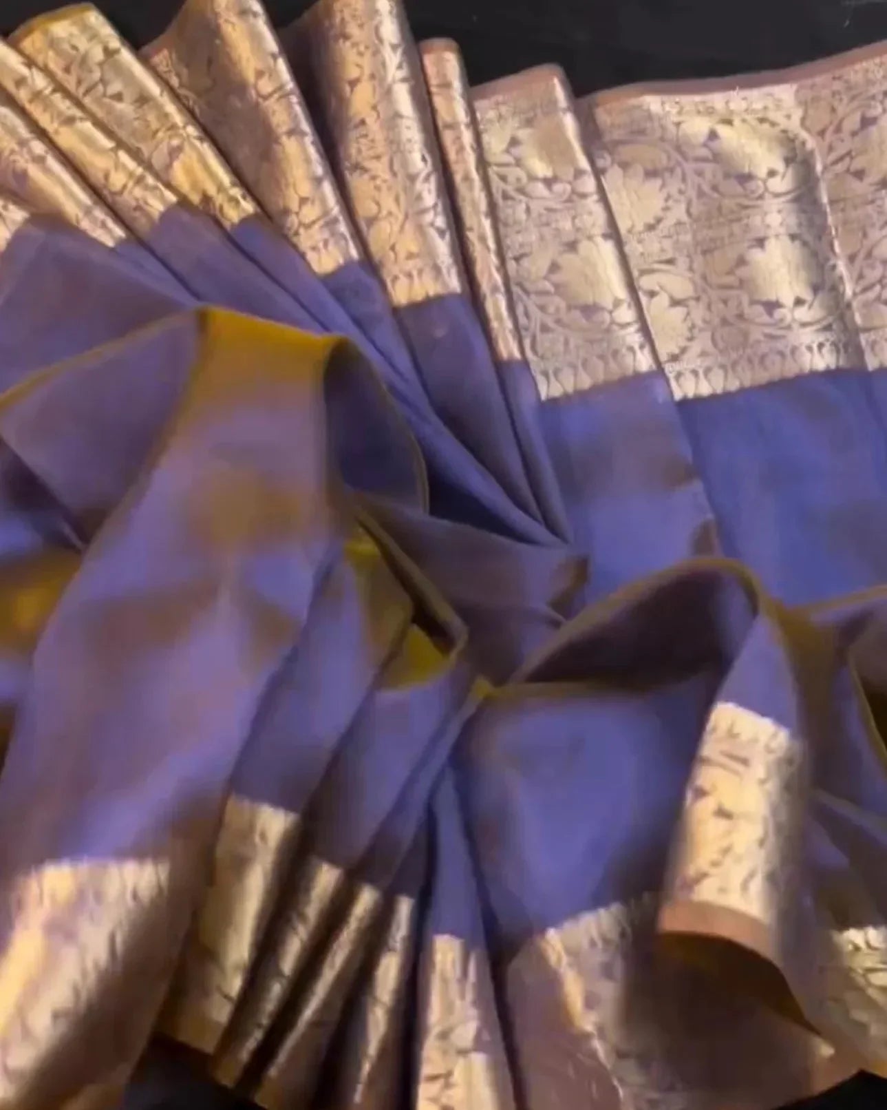 a draped purple saree with ornate gold zari floral patterns on the border, displayed against a dark background.