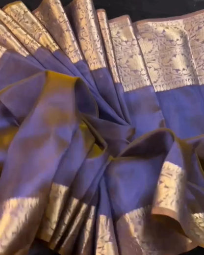 A draped purple saree with ornate gold zari floral patterns on the border, displayed against a dark background.