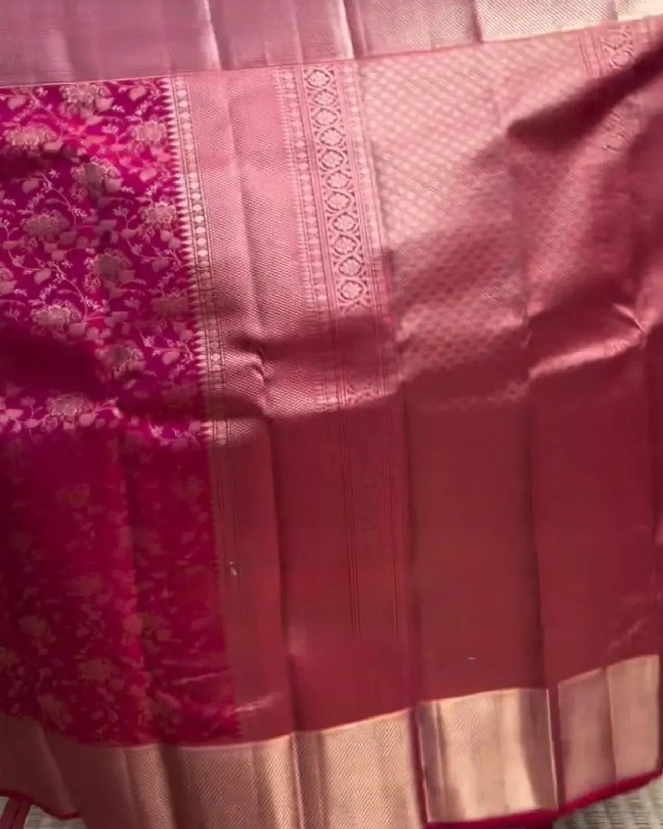 person holding a pink saree with a patterned border in a store setting.