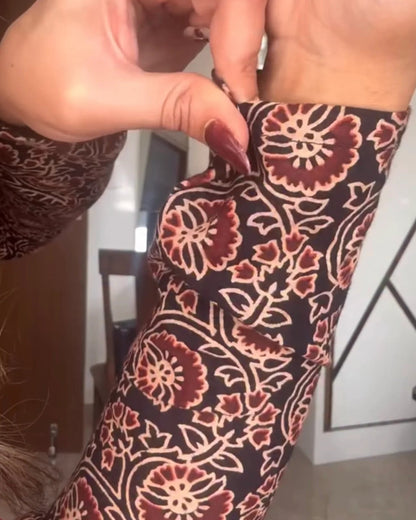 A close-up of a person's forearm wearing a long-sleeve sleeve with a dark brown, burgundy, and beige floral block-print pattern, while another hand adjusts the cuff.