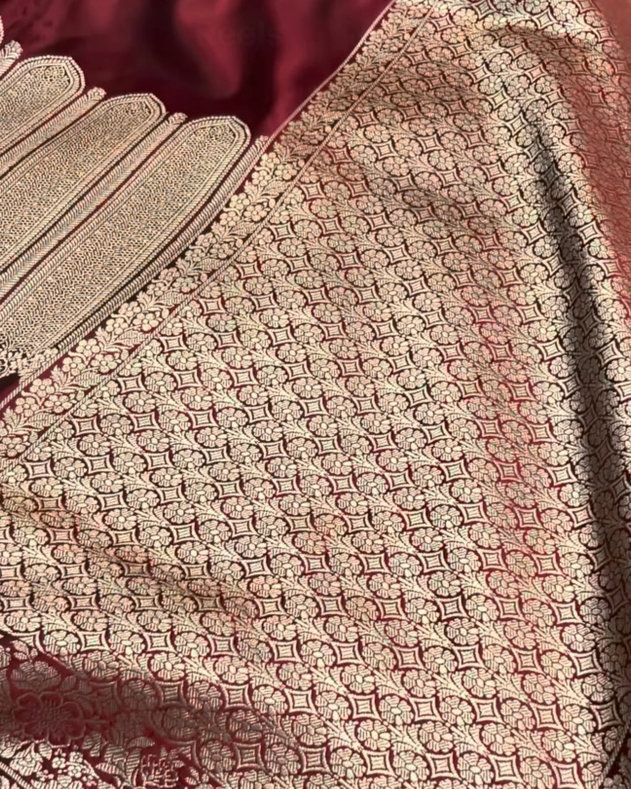 A close-up of a traditional Indian saree fabric, featuring a deep maroon body with an intricate gold zari woven pattern and a wide matching border.