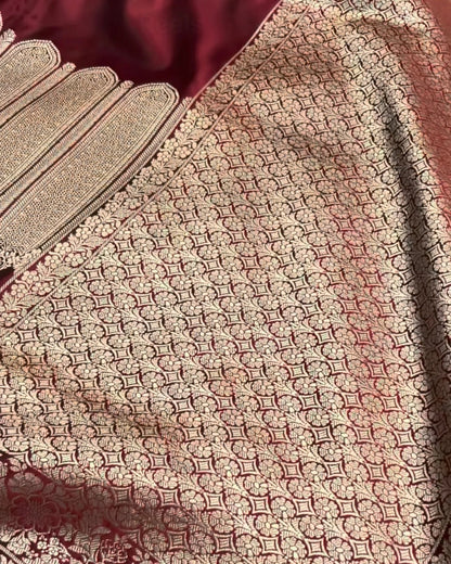 A close-up of a traditional Indian saree fabric, featuring a deep maroon body with an intricate gold zari woven pattern and a wide matching border.