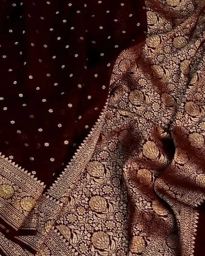 A close-up of a dark maroon or burgundy fabric with dense metallic gold woven floral patterns and small gold dots, likely a textile or scarf.