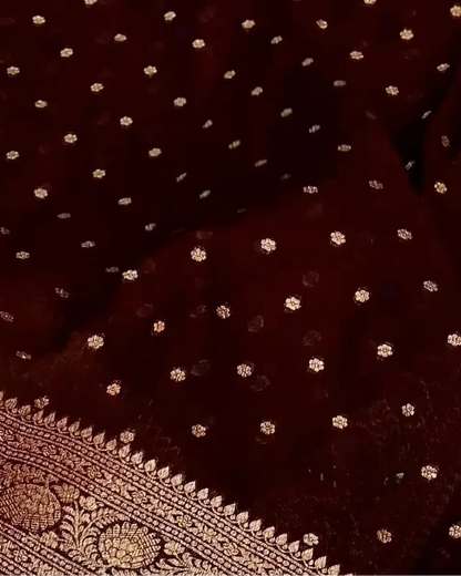 A close-up of a deep maroon or burgundy fabric with small scattered metallic gold floral motifs and a decorative gold border pattern visible along the lower edge.