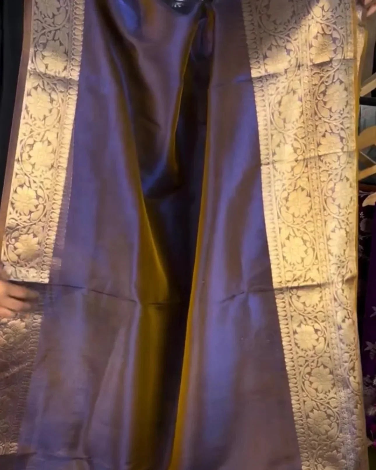 a draped purple silk saree with ornate gold zari floral patterns along the borders, shown in a close-up view.