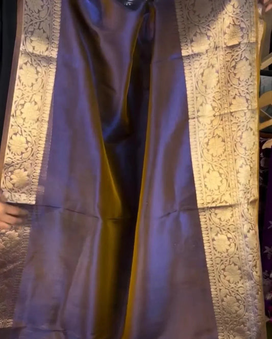 A draped purple silk saree with ornate gold zari floral patterns along the borders, shown in a close-up view.