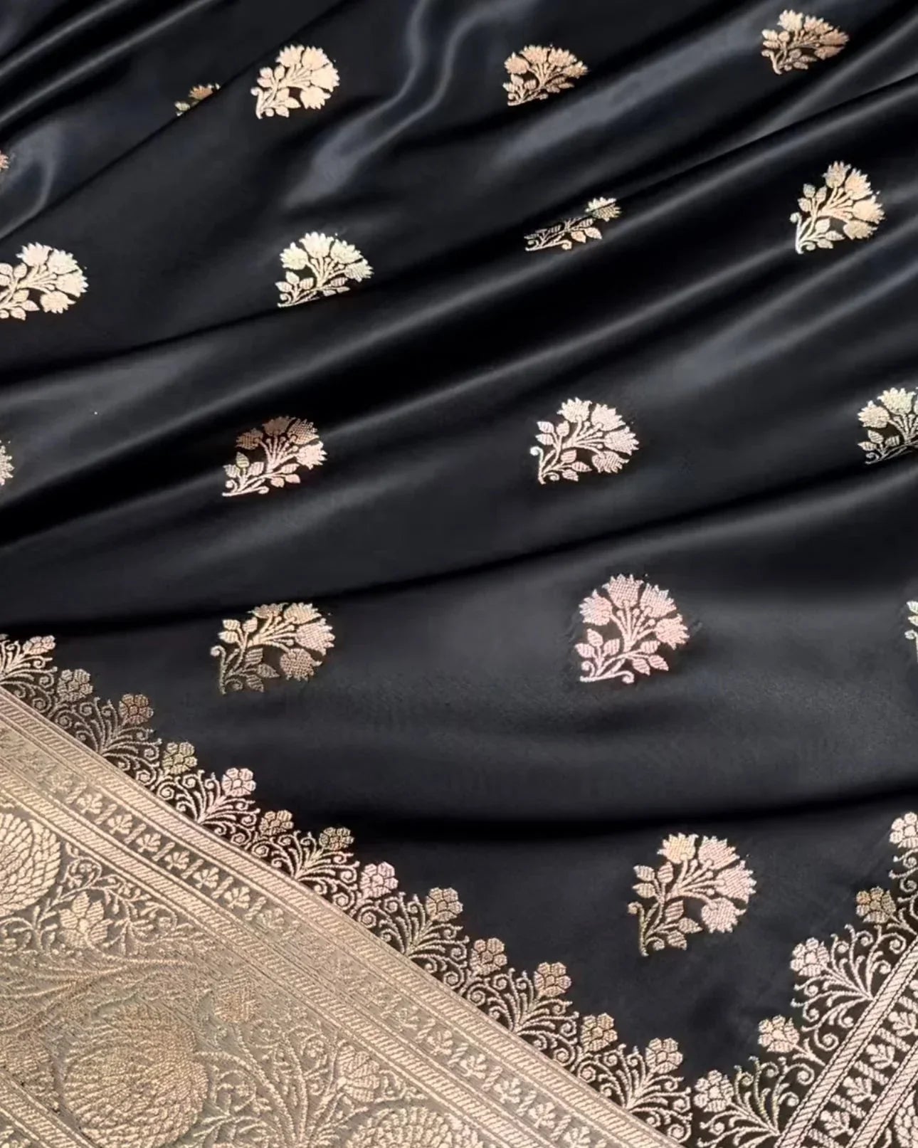 a close-up of a black silk saree or fabric with metallic gold floral motifs and a detailed gold border.