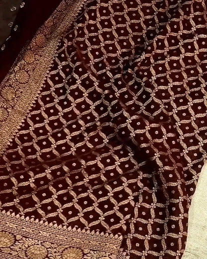 A close-up of a dark brown brocade fabric with an intricate gold geometric lattice pattern and a heavily embroidered border.