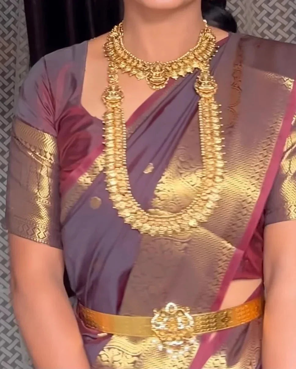 a close-up of a person wearing a traditional sari with a deep purple body, rich gold zari metallic patterns, and a matching gold waist belt, accessorized with a heavy gold necklace.