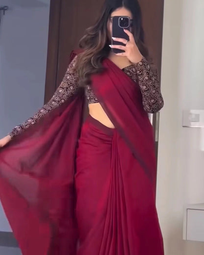 A woman takes a mirror selfie wearing a deep red sari with sheer black patterned sleeves and a side cutout, holding out one side of the drape.