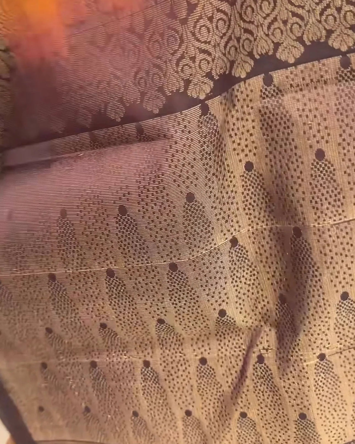 A close-up of a patterned fabric, likely a saree, featuring a beige and black floral design with a metallic gold border.