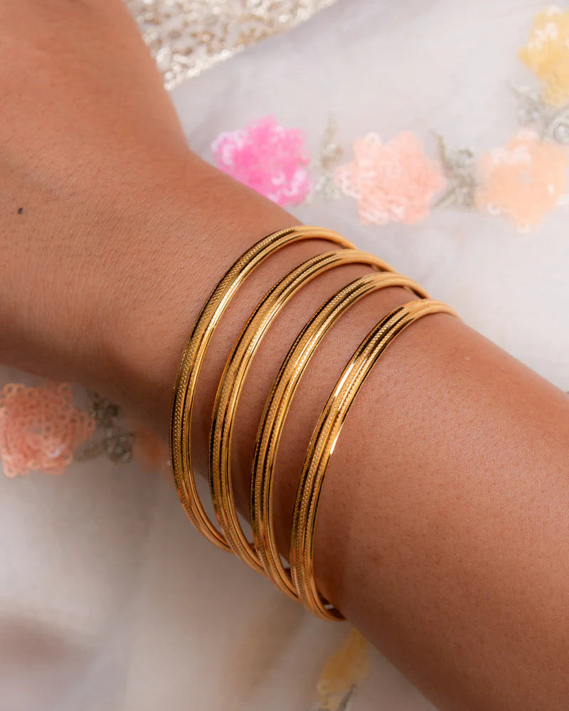 Gold bangles on a wrist with a floral background