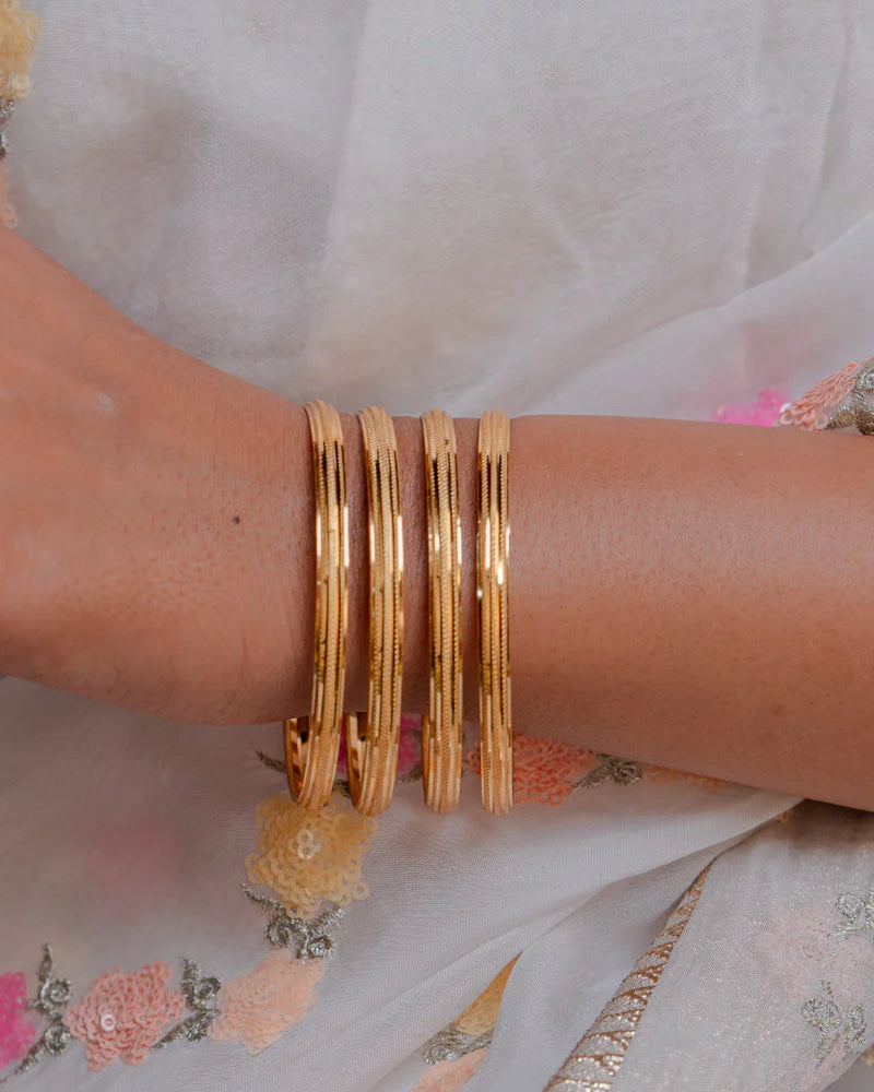 Gold bangles on a wrist with a floral dress in the background