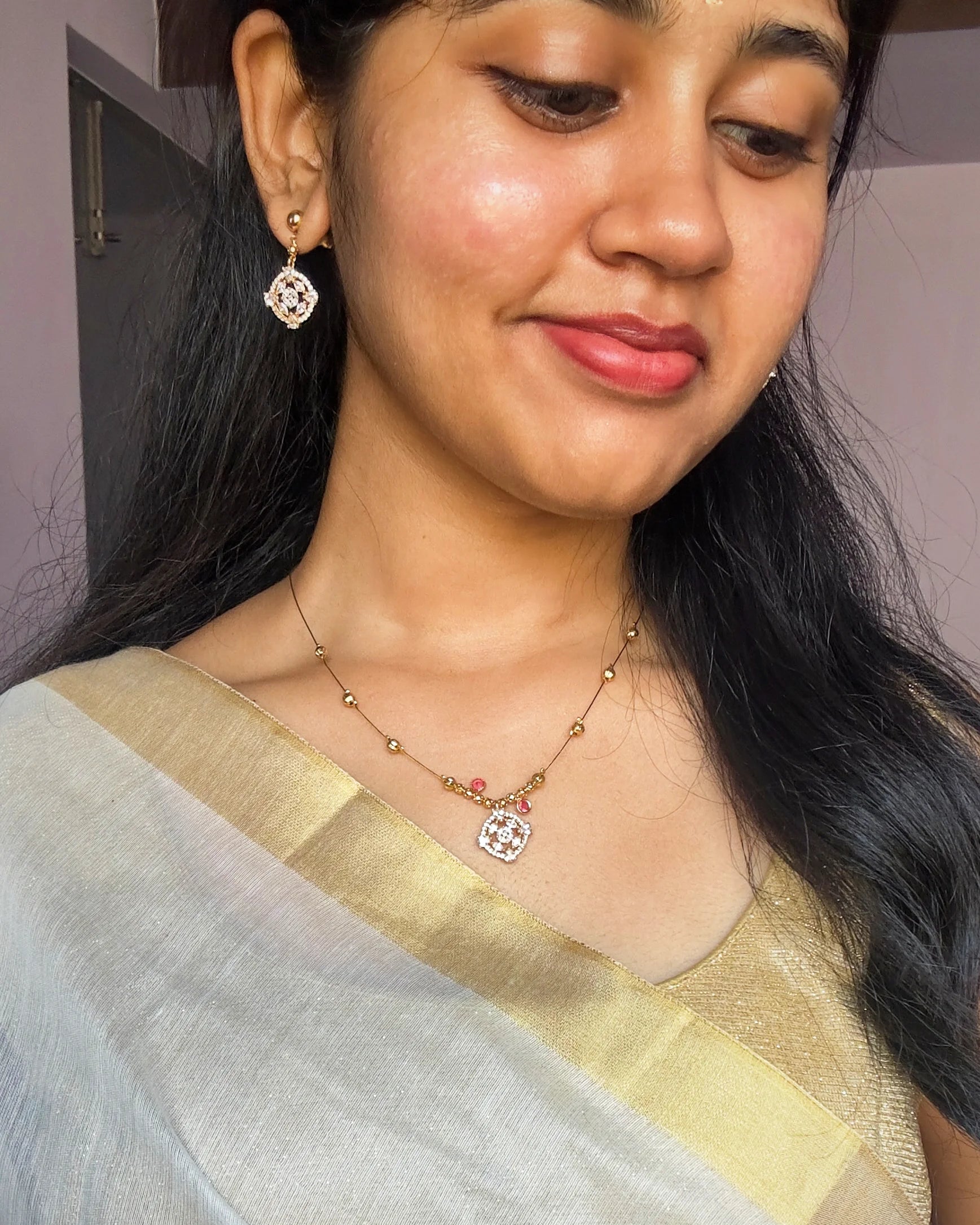 Woman wearing a light-colored saree with a necklace and earrings indoors.
