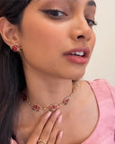 Woman wearing a necklace and earrings with a pink top against a neutral background